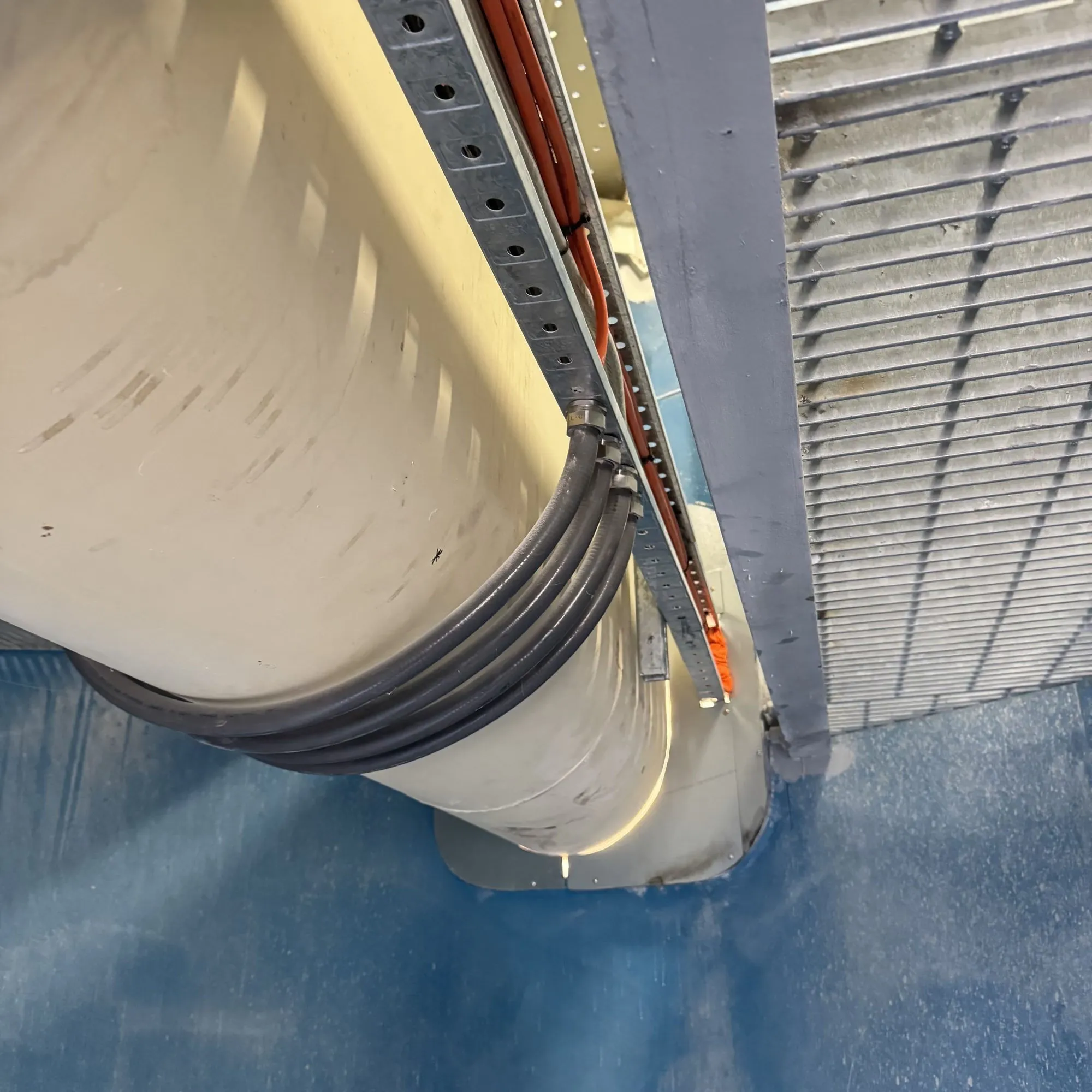 Bundle of black cables clipped around a silo cone below a support rail on a blue-painted deck