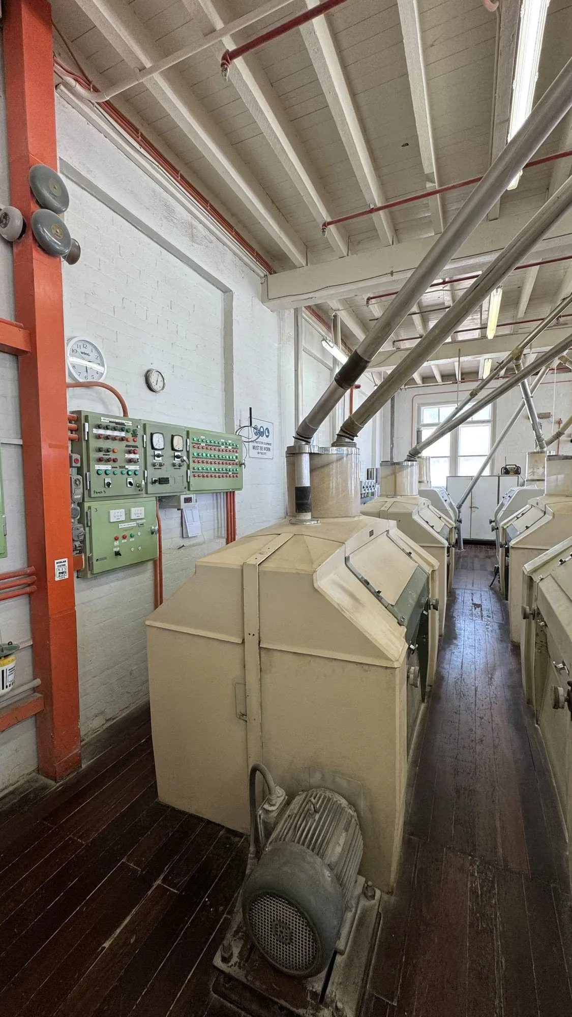 Green control panel mounted on the wall of a flour mill floor, roller mills and ducting alongside