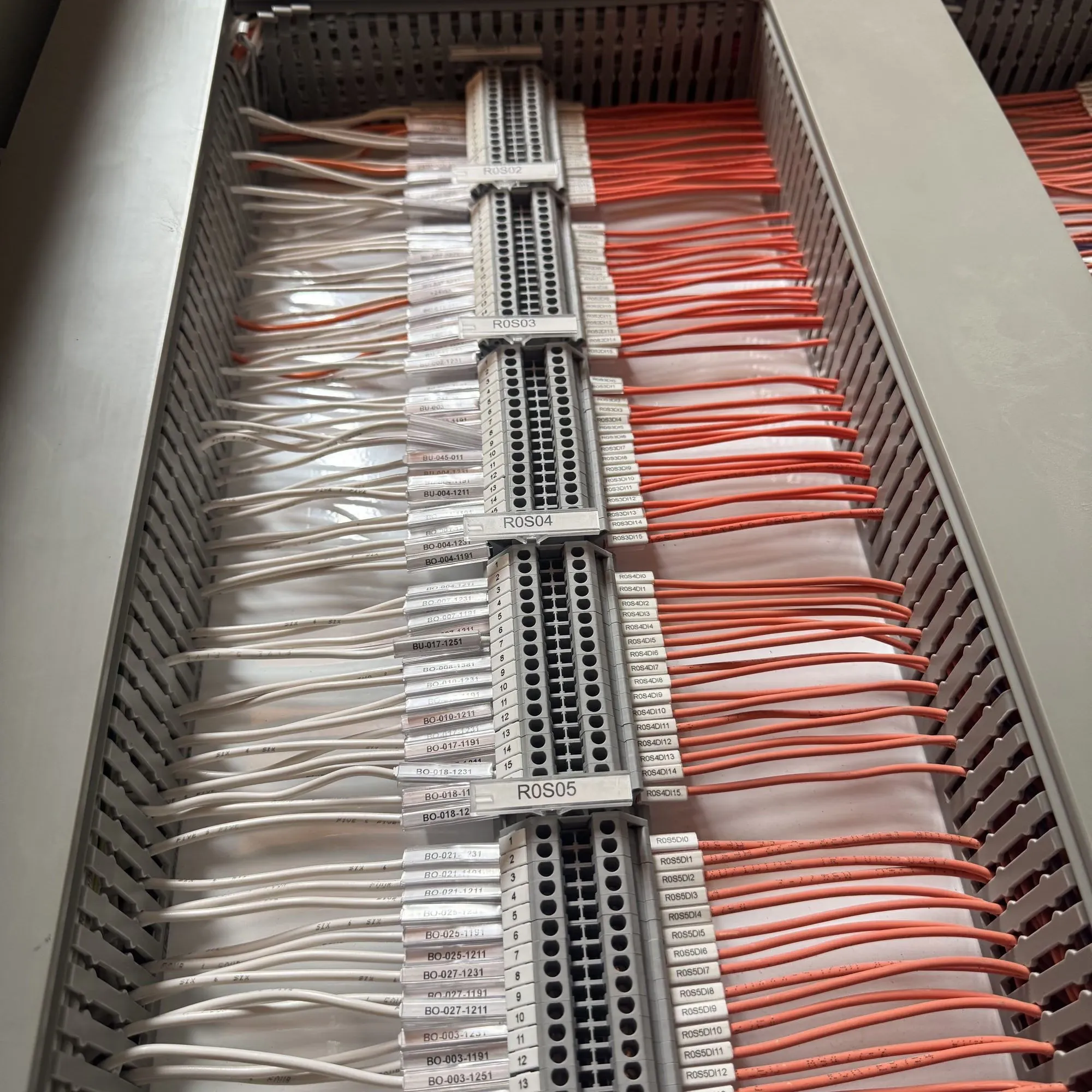 Numbered terminal blocks in a panel wiring duct, white conductors one side and orange the other