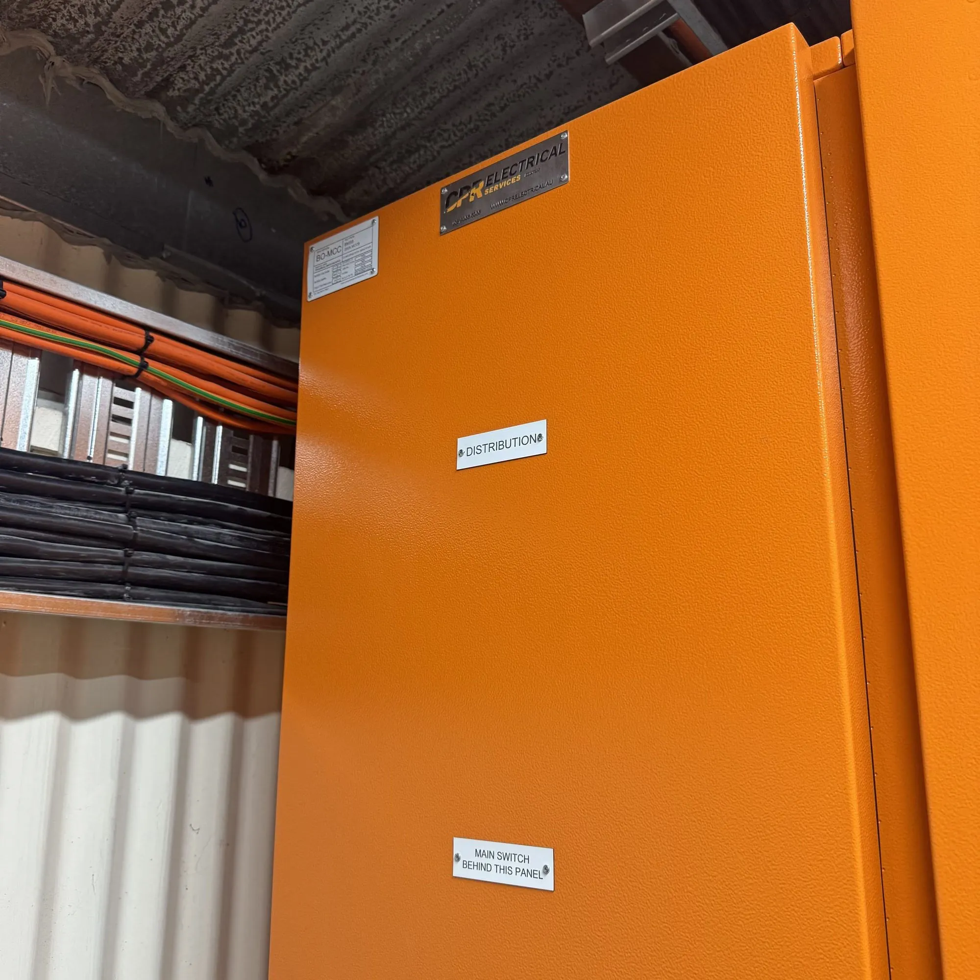 Orange distribution board with a CPR Electrical badge installed in a plant room, cabling on tray behind