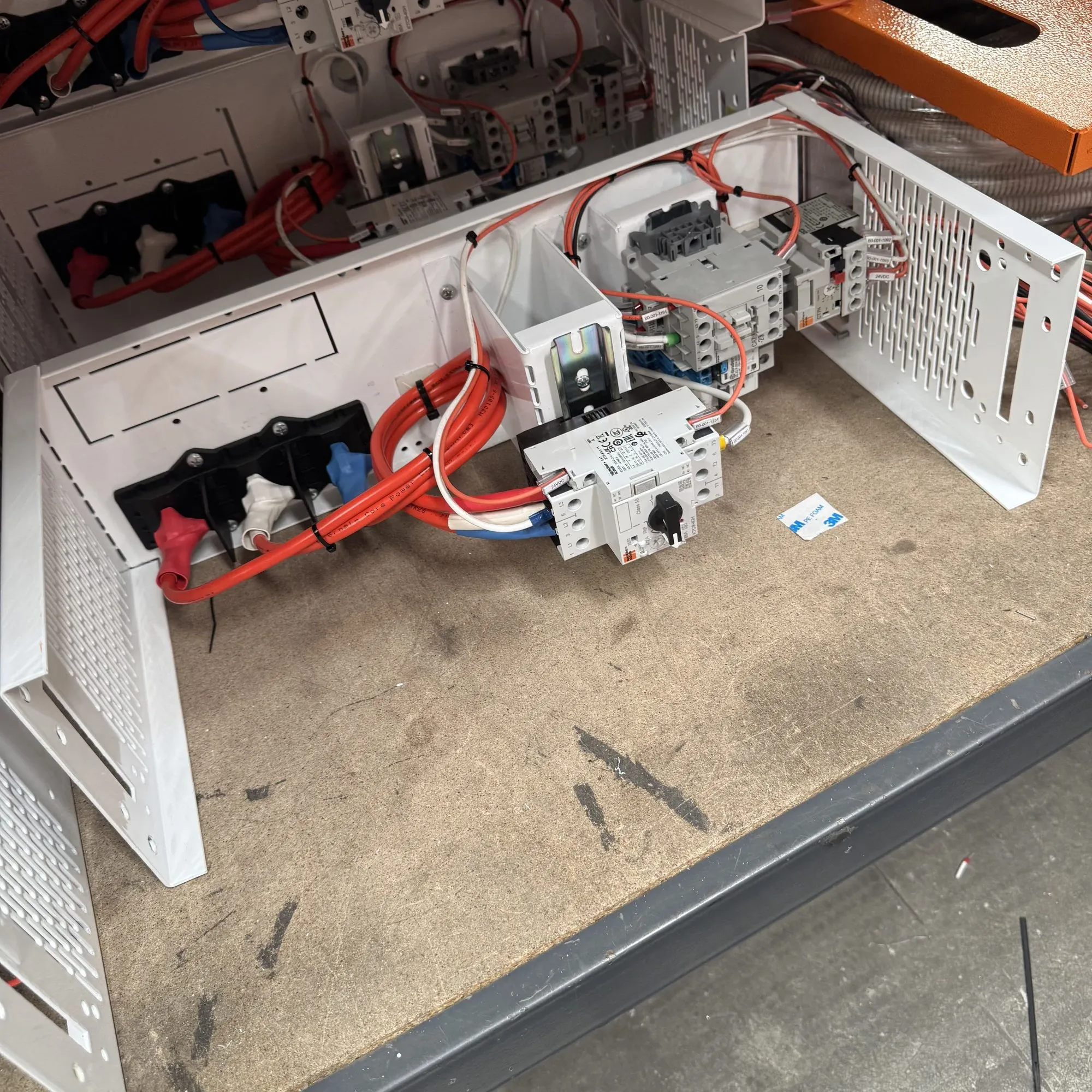 Part-wired switchboard chassis on a workbench with red conductors, DIN-rail protective devices and links