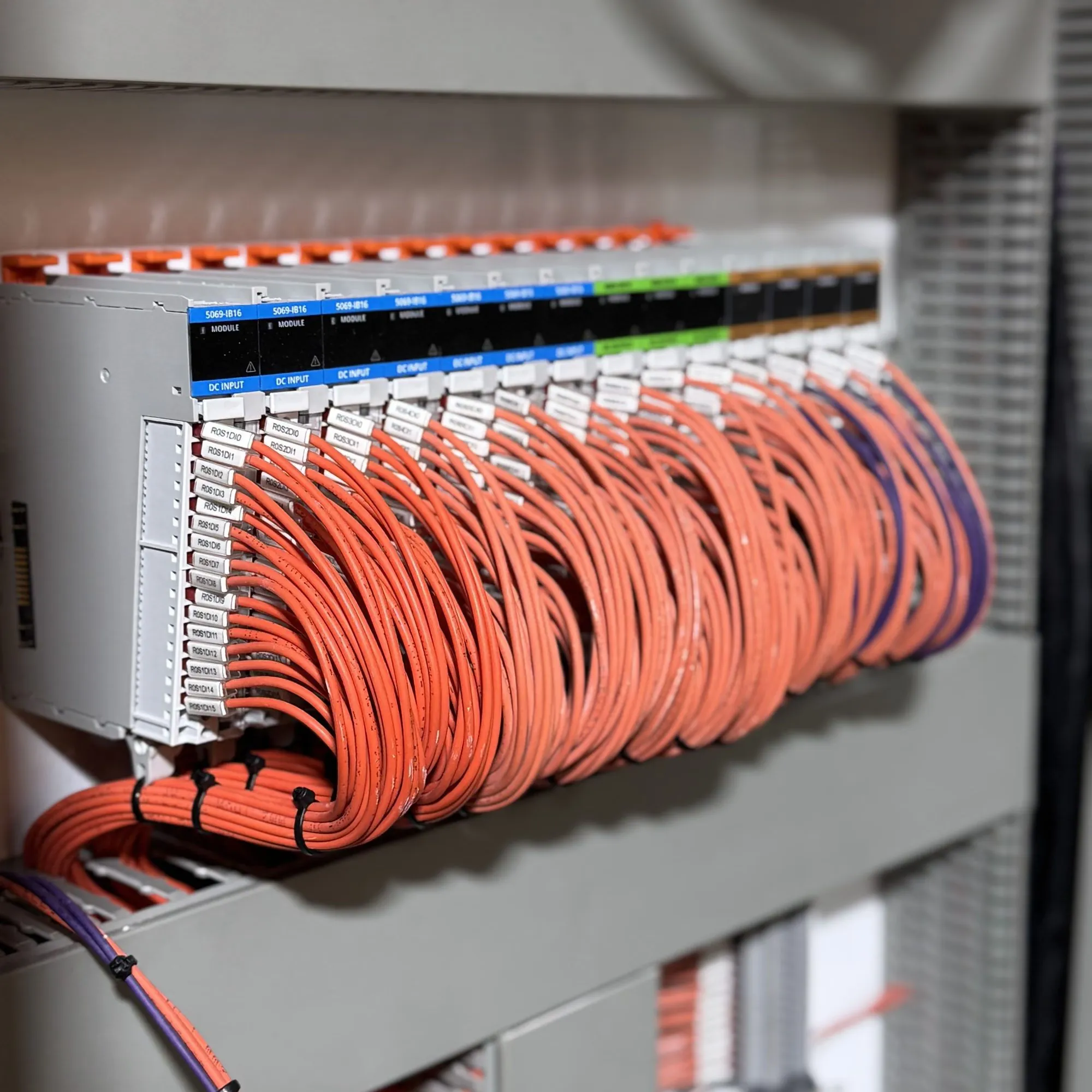 PLC input rack seen from the side, orange field cables looped and cable-tied down into the panel gutter