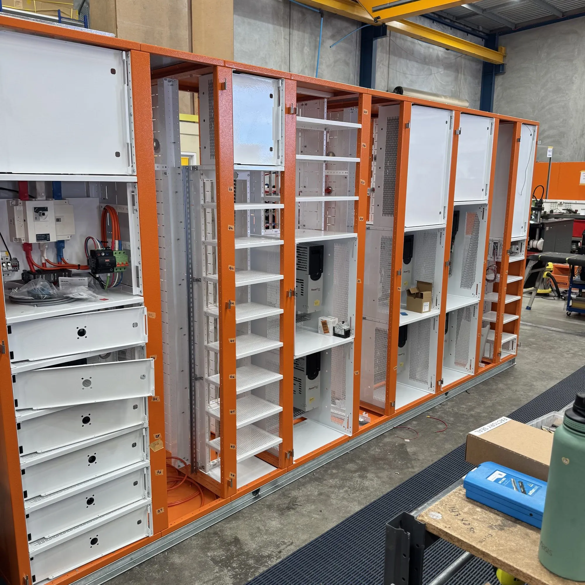 Row of orange switchboard cubicles under assembly in the workshop, gear plates in and doors removed